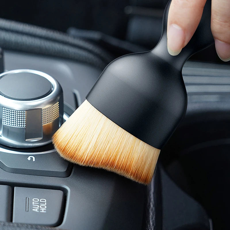 Eine Hand hält eine schwarze und natürliche Borstenbürste für Auto-Lüftungsöffnungen.