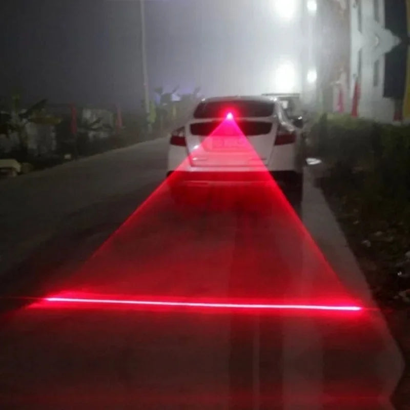A red laser light beam illuminates a road in the dark, directed towards a car.