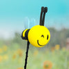 A yellow bee-shaped antenna decoration with blue wings and a black stem against a blurred green background.