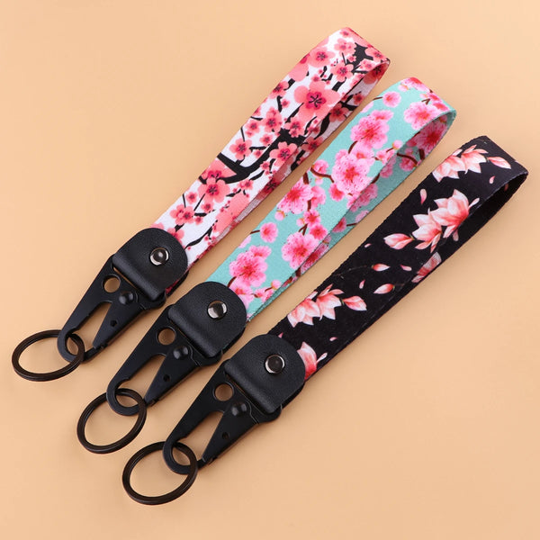 A pink and green floral patterned double-sided phone wrist strap lanyard shown diagonally on a light background.