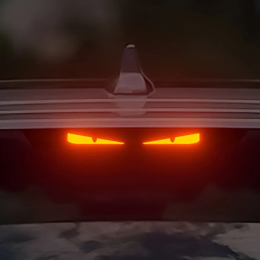 Gros plan d'un feu arrière orange de voiture avec un spoiler noir visible à l'arrière.