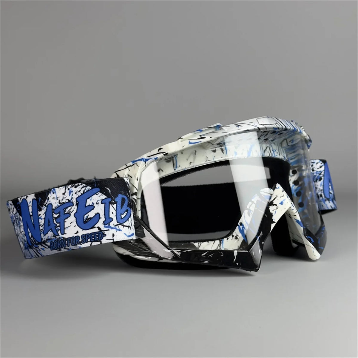 A pair of black and white motorcycle off-road goggles with blue text branding resting on a gray surface.