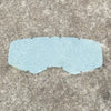 A translucent light blue safety shield or visor for motorcycle or outdoor goggles placed on a gray textured surface.