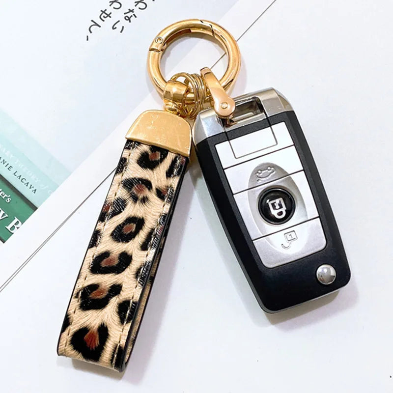 Llavero con anillo dorado y correa de cuero estampado de serpiente leopardo negra y marrón, unido a un dispositivo electrónic