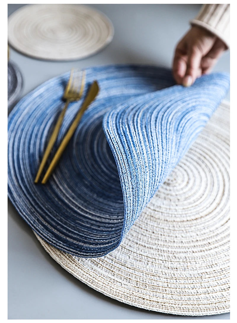 A blue knitted placemat made of cotton yarn is shown next to a light beige woven mat and a gold fork.