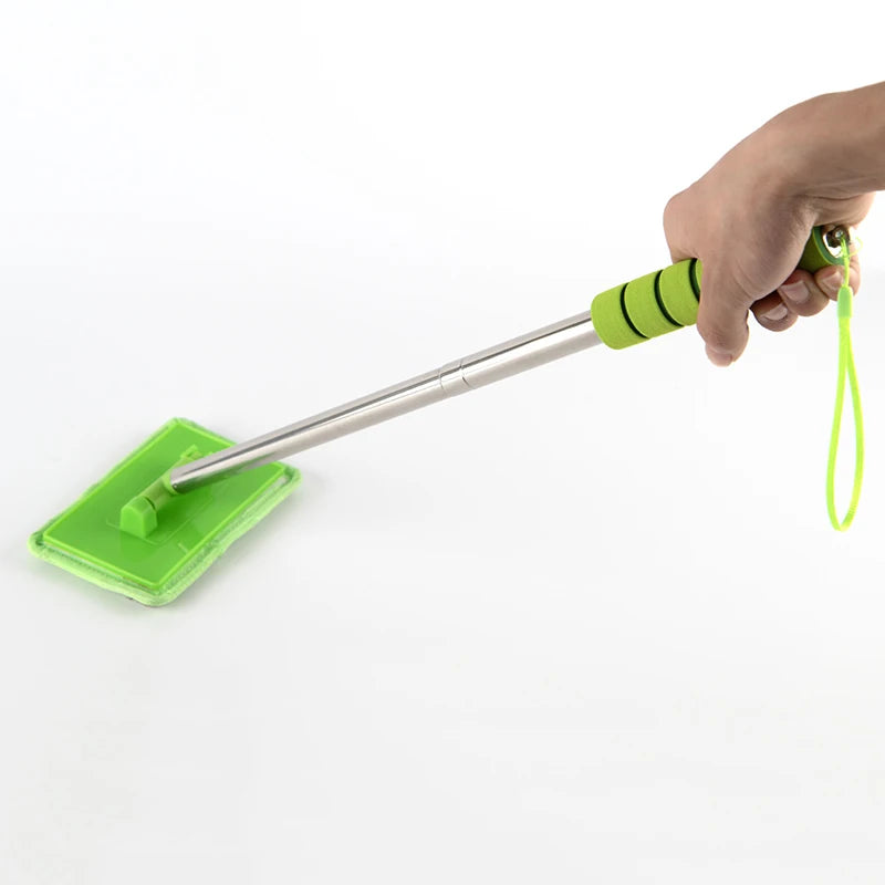 A hand holds a telescopic windshield cleaning brush with a green head and silver shaft against a white background.