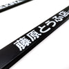 A close-up of a black license plate frame decoration with white Japanese text on a white background.