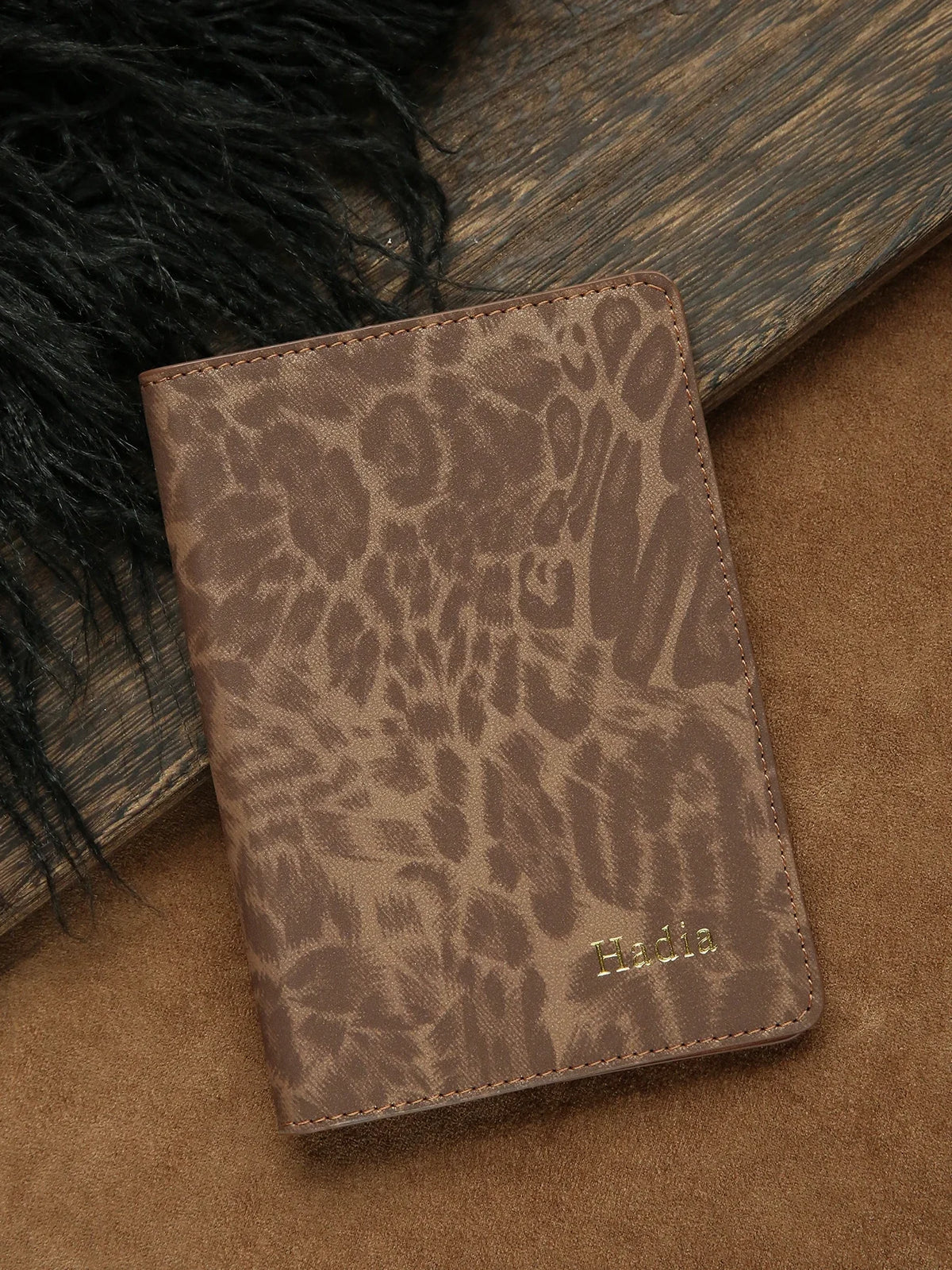 A brown leather passport holder with a leopard print design rests on a tan surface next to black fur.