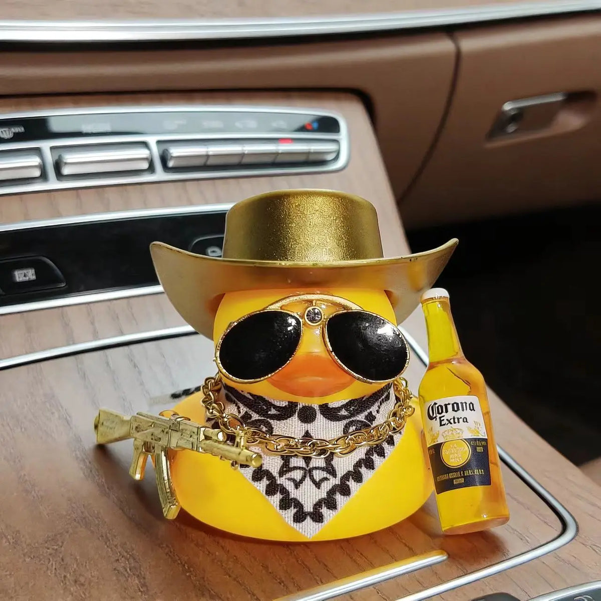 A yellow rubber duck car ornament with gold accents sits on a car dashboard.