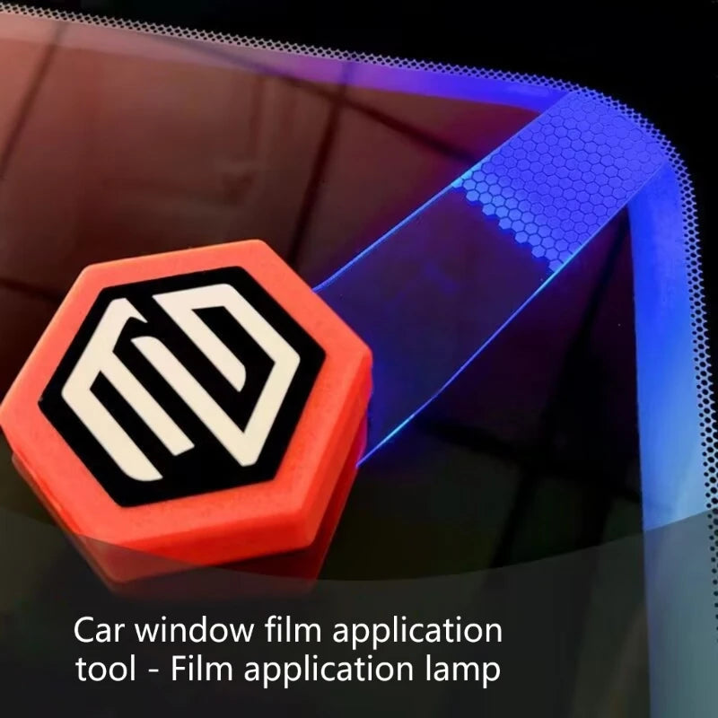 Sechseckiges orangefarbenes Werkzeug mit weißem Logo, beleuchtet durch blaues Licht, zum Anbringen von Autofensterfolie.