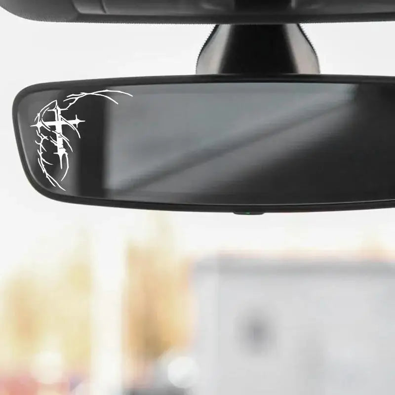 A close-up view of a black car decal set featuring a white gothic thorn cross design mounted on a rearview mirror.