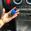 A hand holds a blue car start button cover and a red button on a vehicle's interior panel.