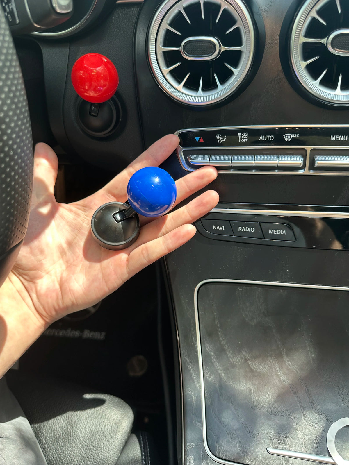 A hand holds a blue car start button cover and a red button on a vehicle's interior panel.