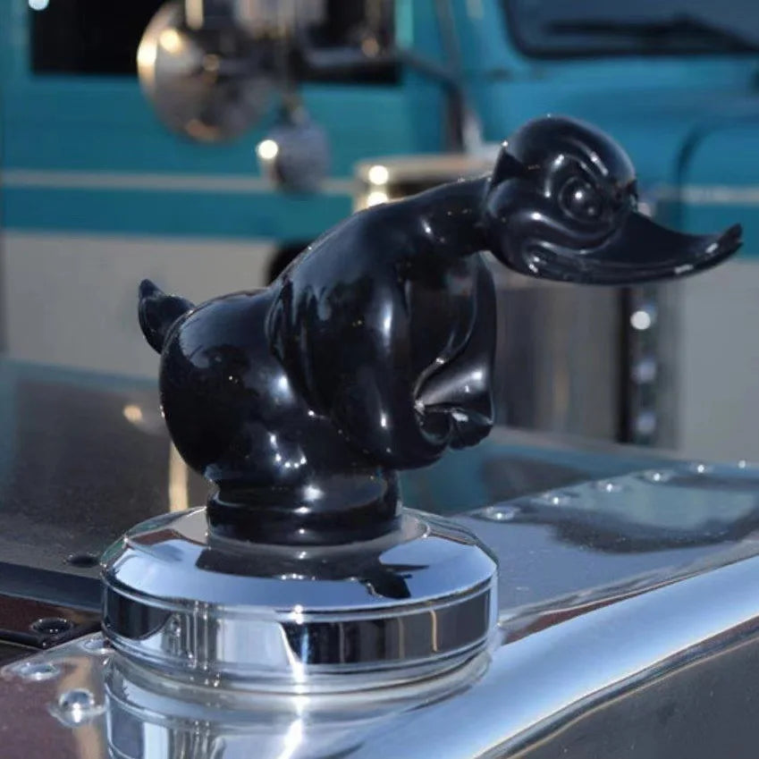 A glossy black decorative angry duck hood ornament resting on a clear glass base.