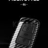 A close-up view of a black carbon fiber style button cover for a car key.