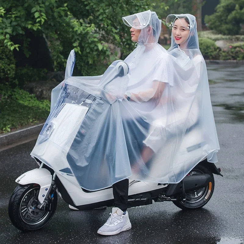 Two women wearing transparent windproof motorcycle rain ponchos ride a white scooter on a wet road.