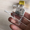 A clear glass car air freshener bottle with a silver mesh top and white wires is held in a hand.