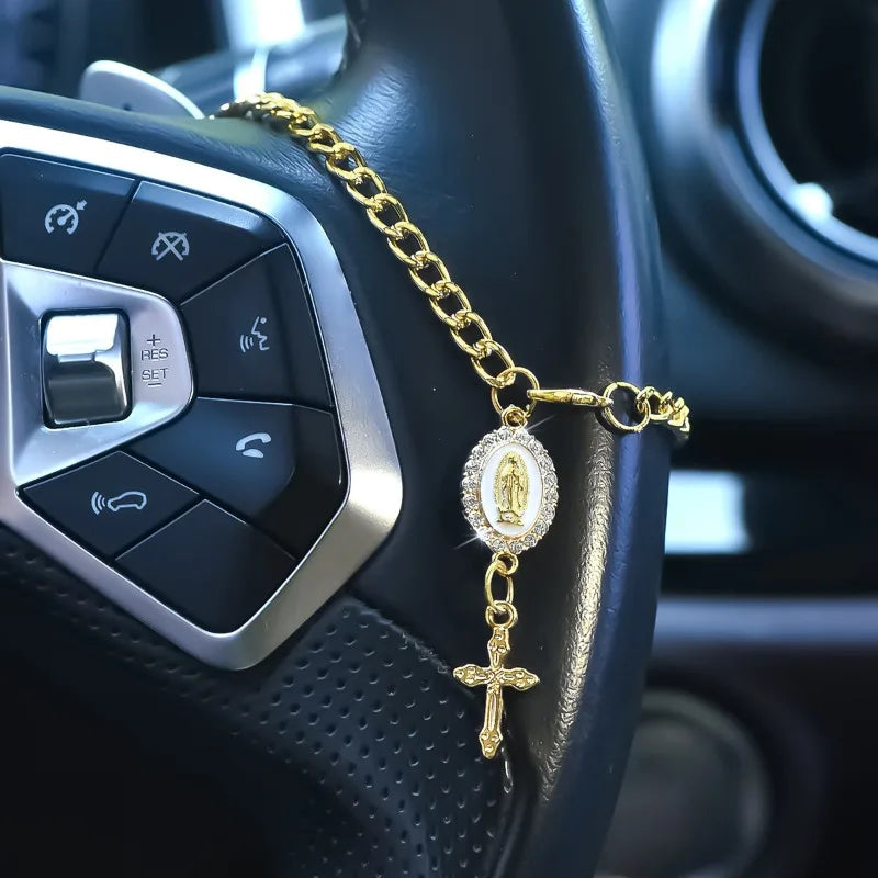 A gold chain rosary with a pendant is draped across the controls of a car steering wheel.