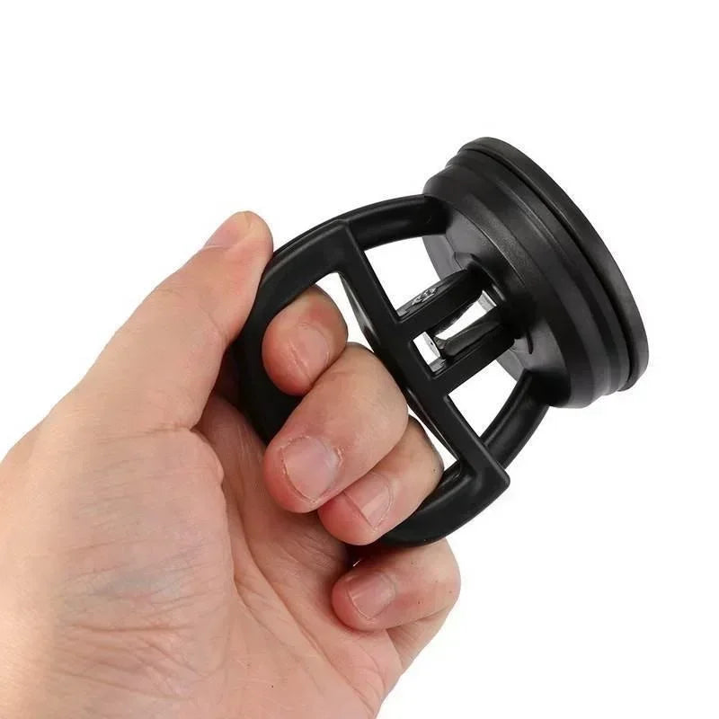 Une main tient un outil tire-dents à ventouse noir et robuste.
