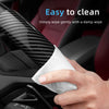 A hand wipes a black carbon fiber steering wheel cover with a white damp wipe for easy cleaning.