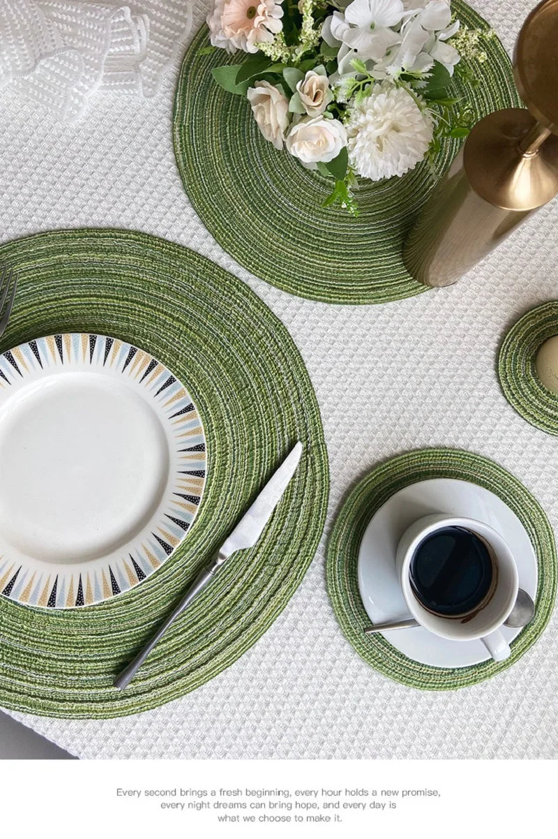 Un ensemble de dessous-de-verre et de sets à couverts tressés ronds vert olive et blanc avec un arrangement floral.