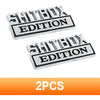 A set of two silver metal logos with the text SHITBOX EDITION for automotive use