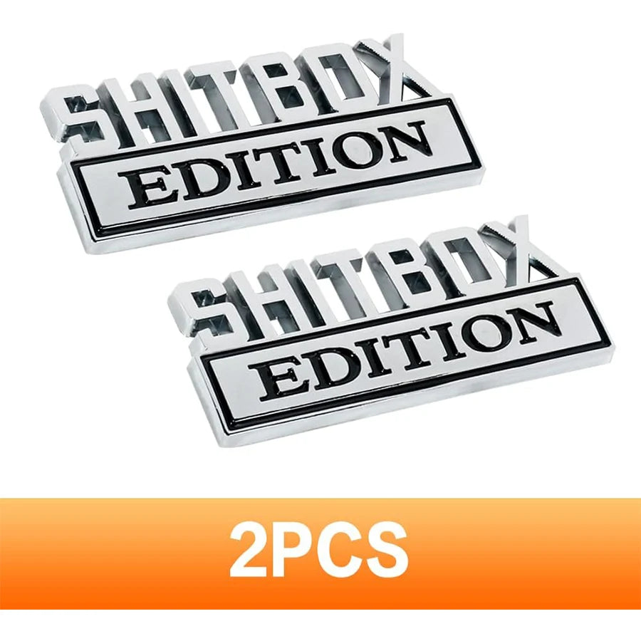 A set of two silver metal logos with the text SHITBOX EDITION for automotive use