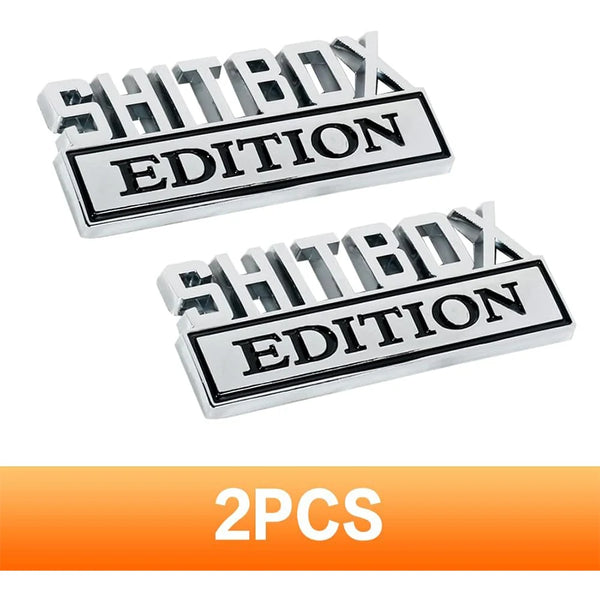 Un juego de dos logotipos metálicos plateados con el texto SHITBOX EDITION para uso automotriz
