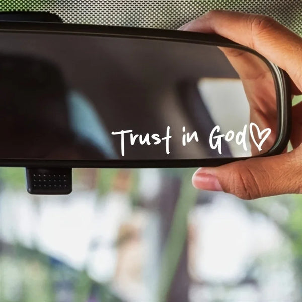A hand holds a faith heart vinyl decal with the words Trust in God on a dark surface.