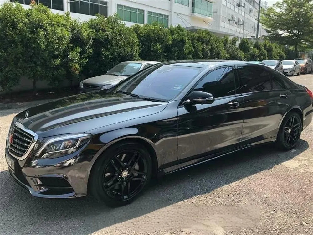 A black Mercedes-Benz sedan parked outdoors with green hedges and other vehicles in the background.