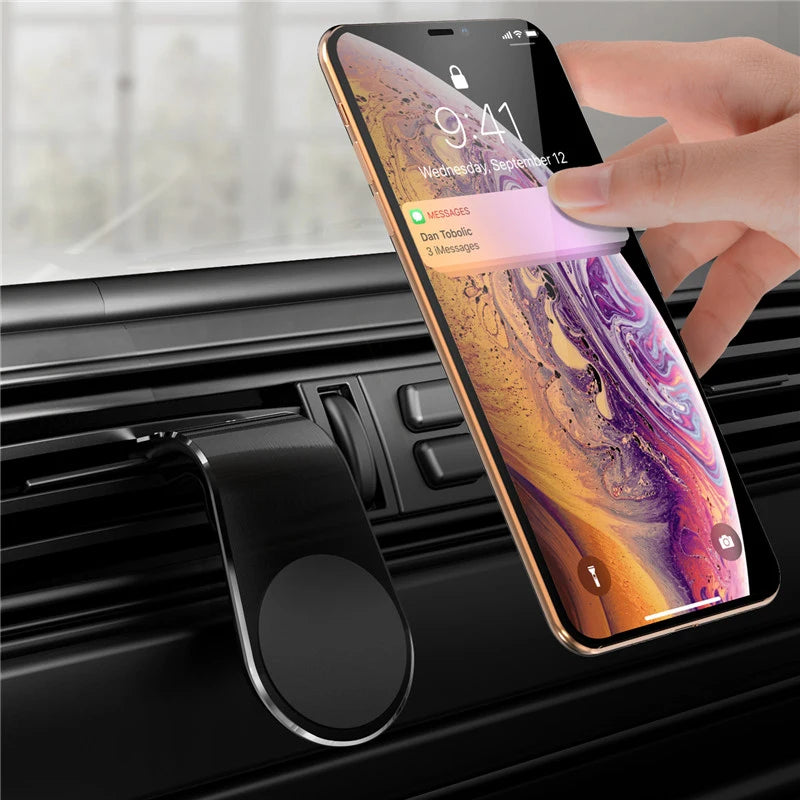 A hand is placing a smartphone into a magnetic car phone mount with an air vent clip.