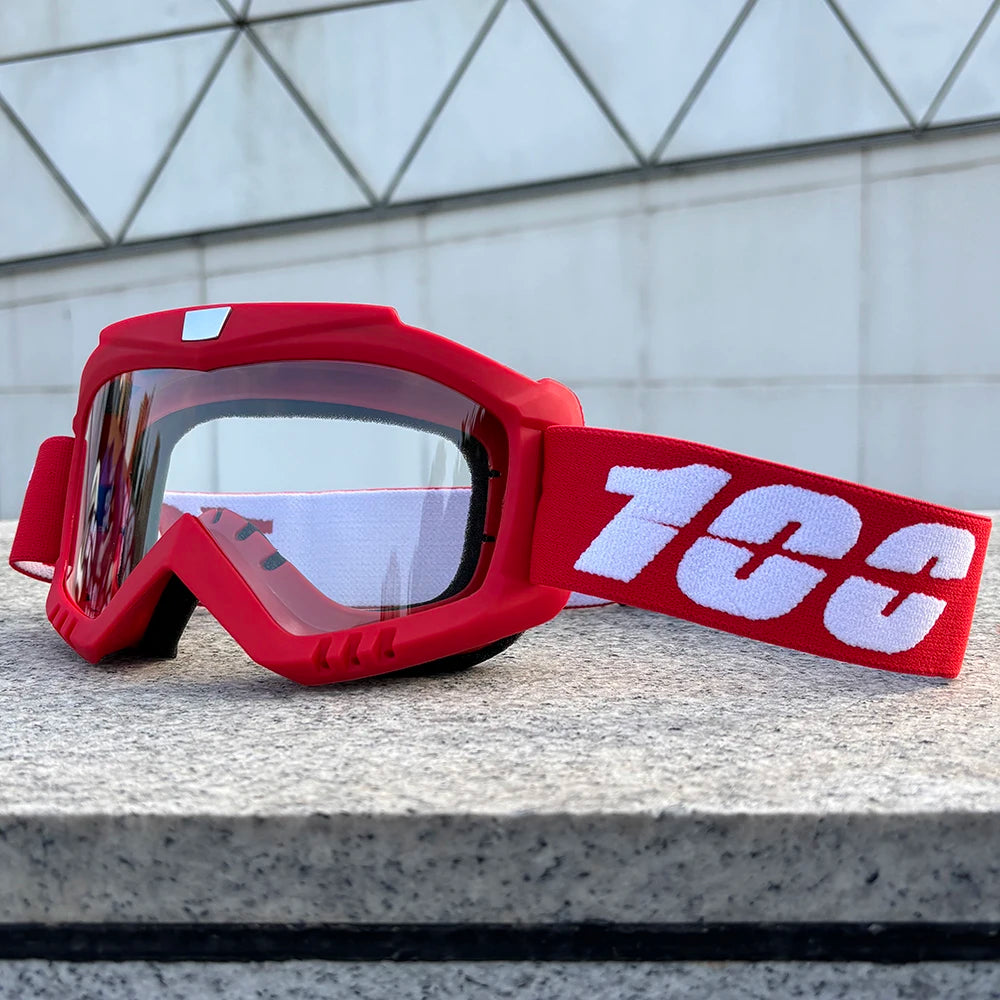 A red windproof sports goggle with a white '100' logo rests on a gray stone surface.