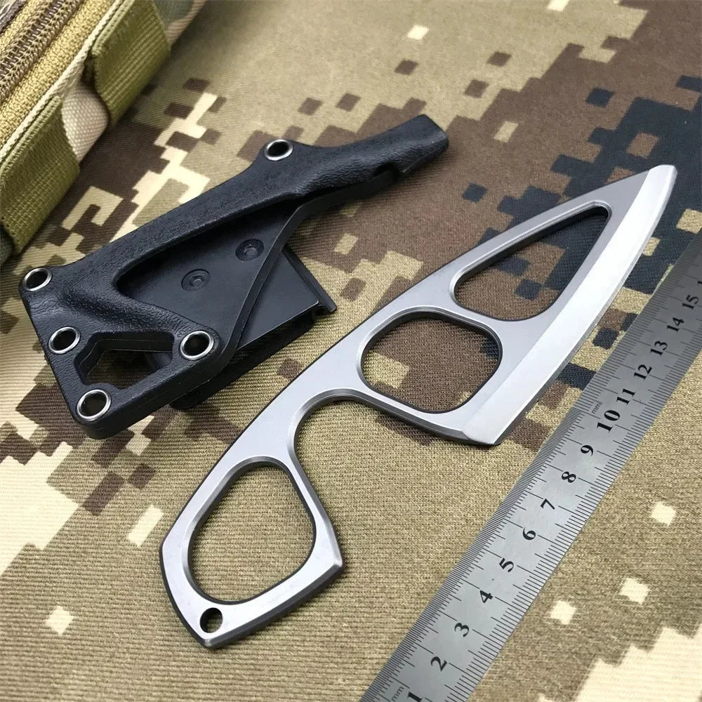 A black fixed blade knife is shown next to a silver blade and a ruler on a camouflage background.