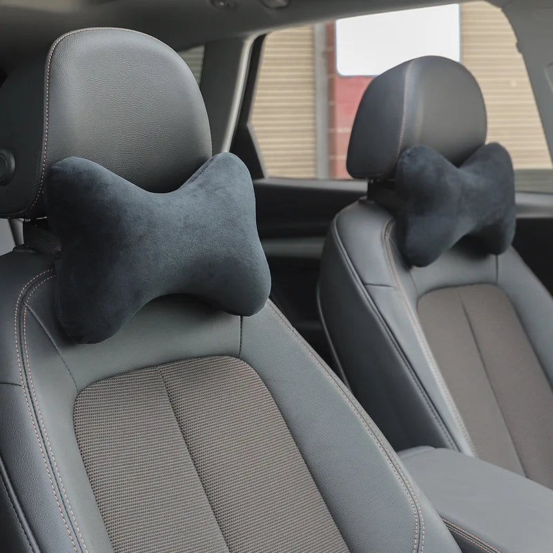 A close-up view of a gray car seat with a black memory foam neck pillow on the headrest.