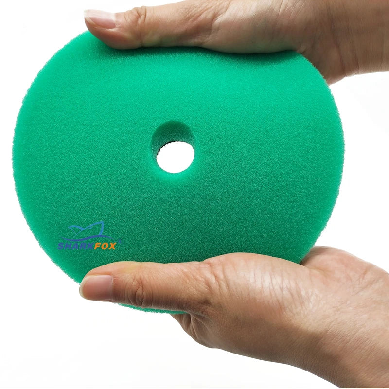 A hand holds a bright green, circular polishing sponge pad with a central hole.
