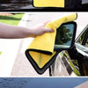 A hand is using a yellow microfiber car washing towel to clean the exterior of a car.