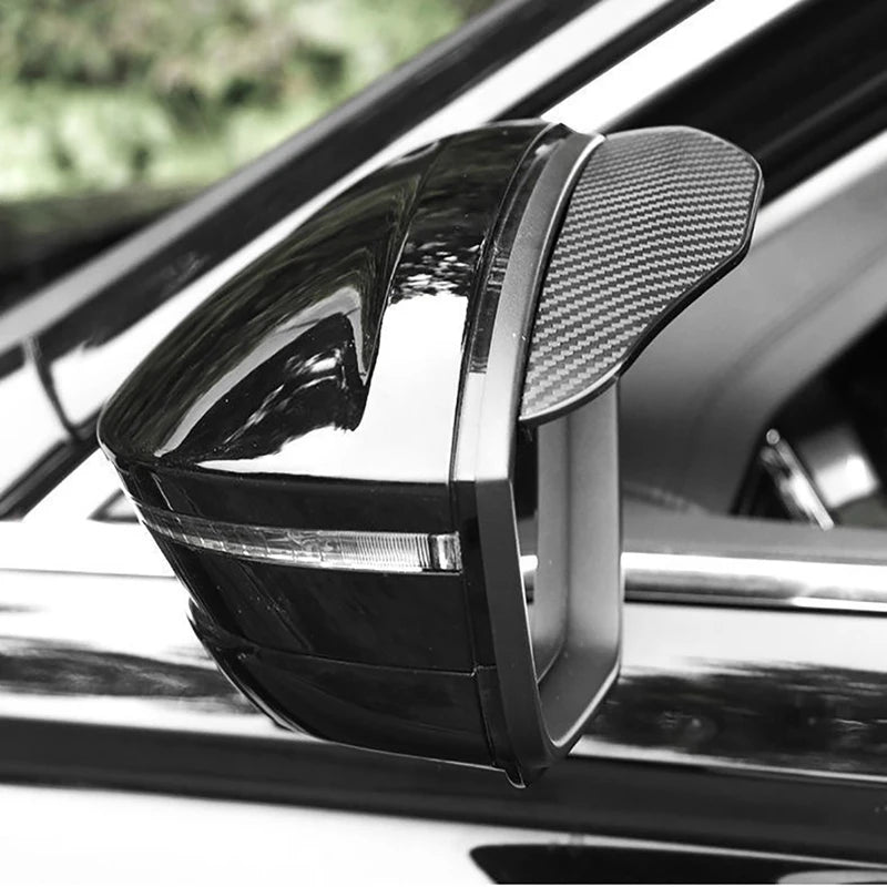 A close-up view of a black universal car rearview mirror rain and dust visor installed on a vehicle.