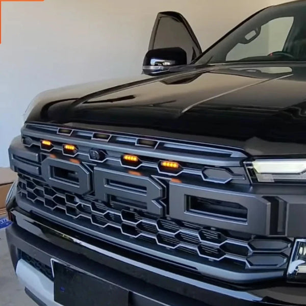 Close-up of a black Ford Ranger Raptor grille with amber LED lights.