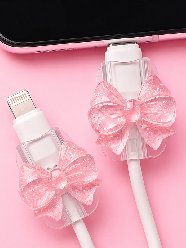 Pink glitter bow cable protectors for lightning and type-c chargers shown on a pink background.