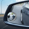 A close-up view of a car's interior rearview mirror showing the exterior road and surrounding environment.
