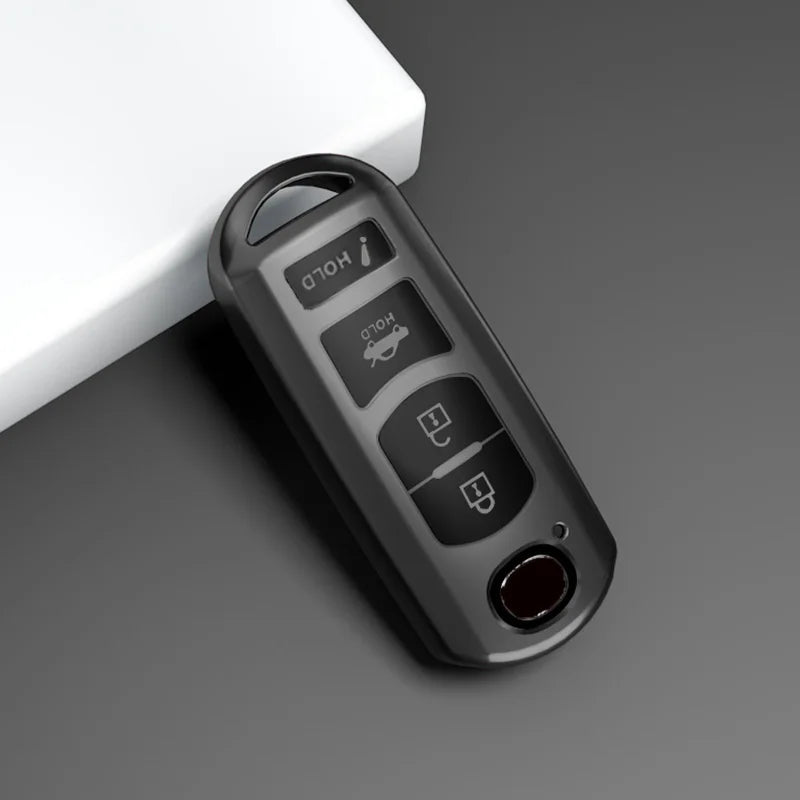 A black universal car key cover with various buttons and a red lens is shown on a gray surface.