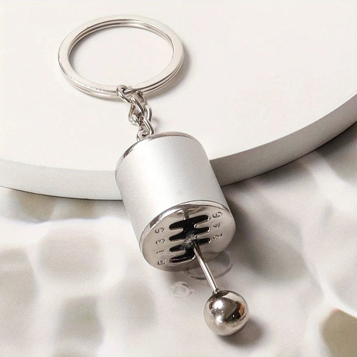 Silver cylindrical keychain with a loop and a spherical charm resting on a white surface.
