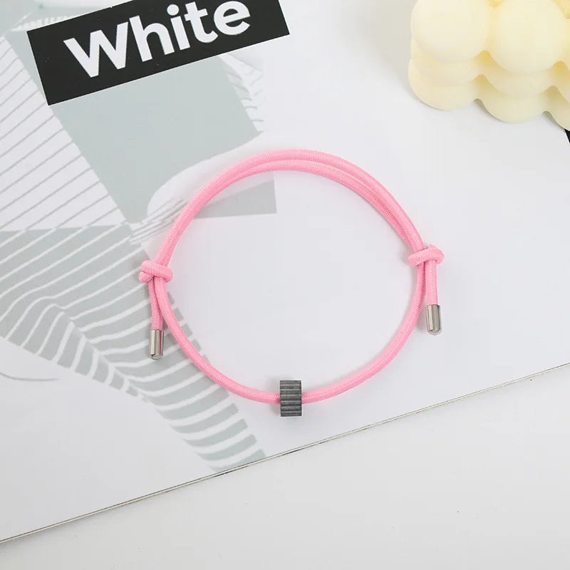 A pink heart-shaped fitness tracker bracelet is displayed on a white background next to a piece of paper.