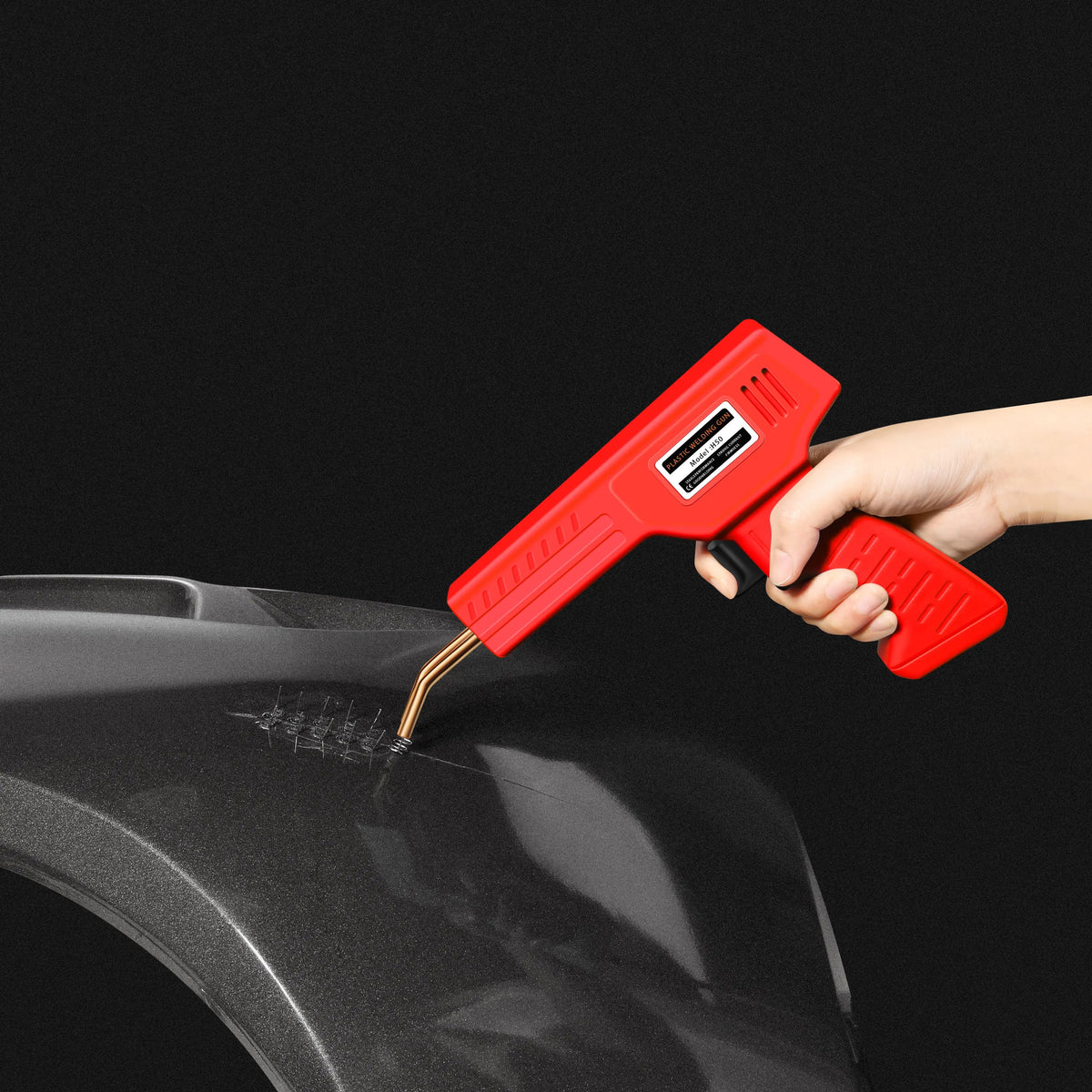 A hand holds a red heavy duty plastic welding and repair kit, applying heat to a black plastic surface.