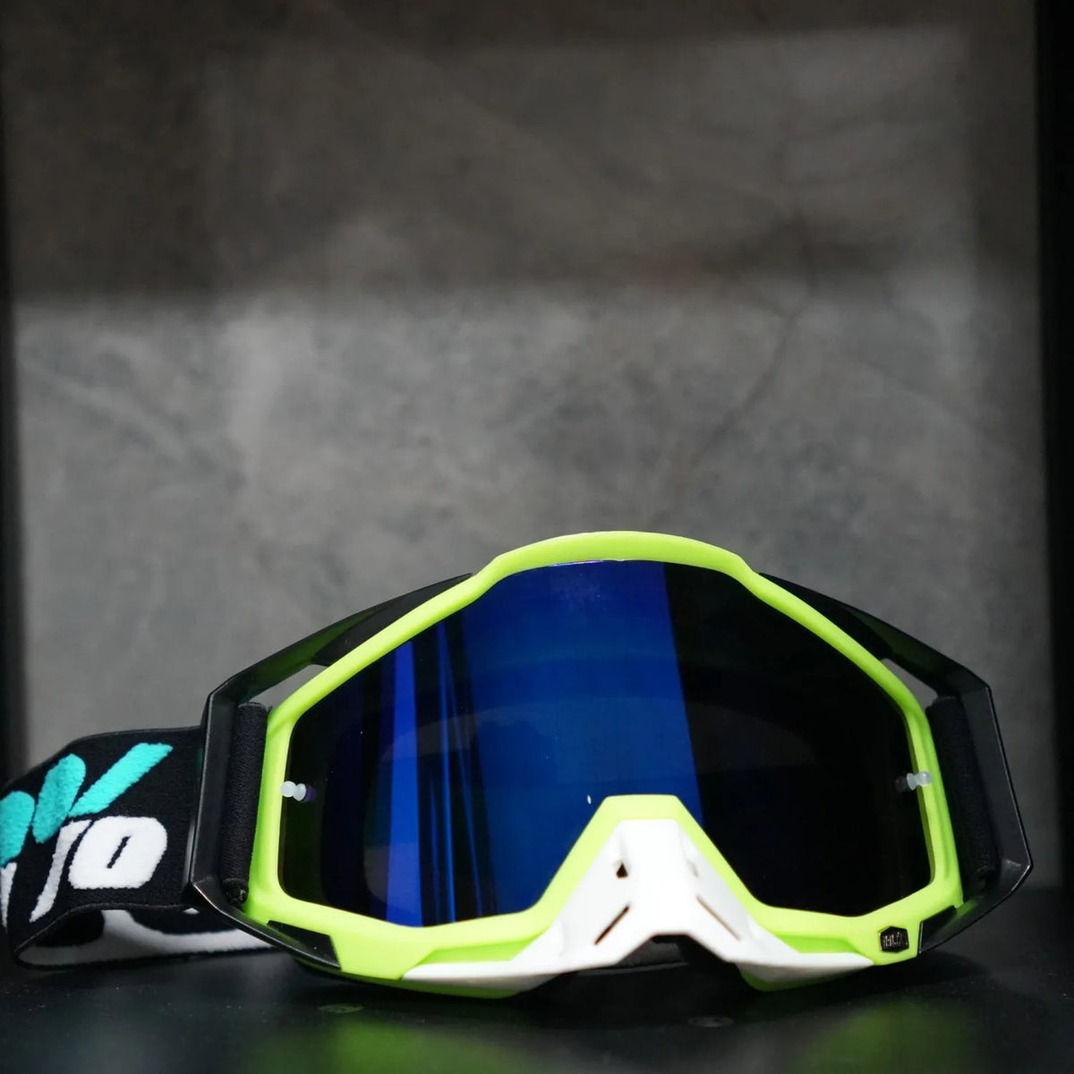 A pair of bright neon green and blue high-performance motocross goggles resting on a dark surface.
