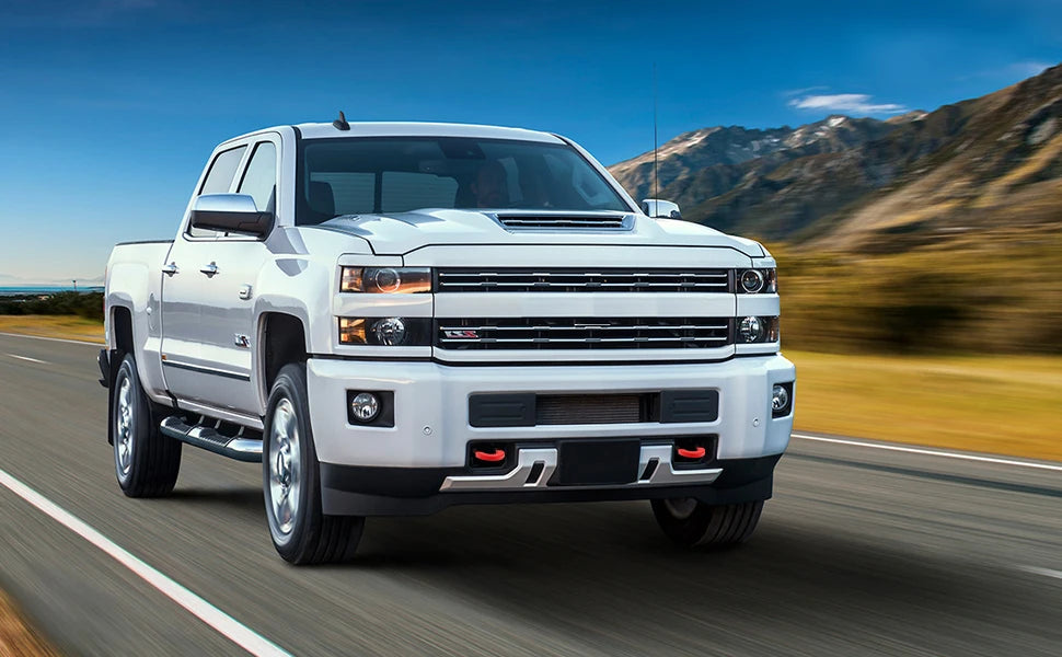 A white pickup truck is driving on a road with mountains in the background.