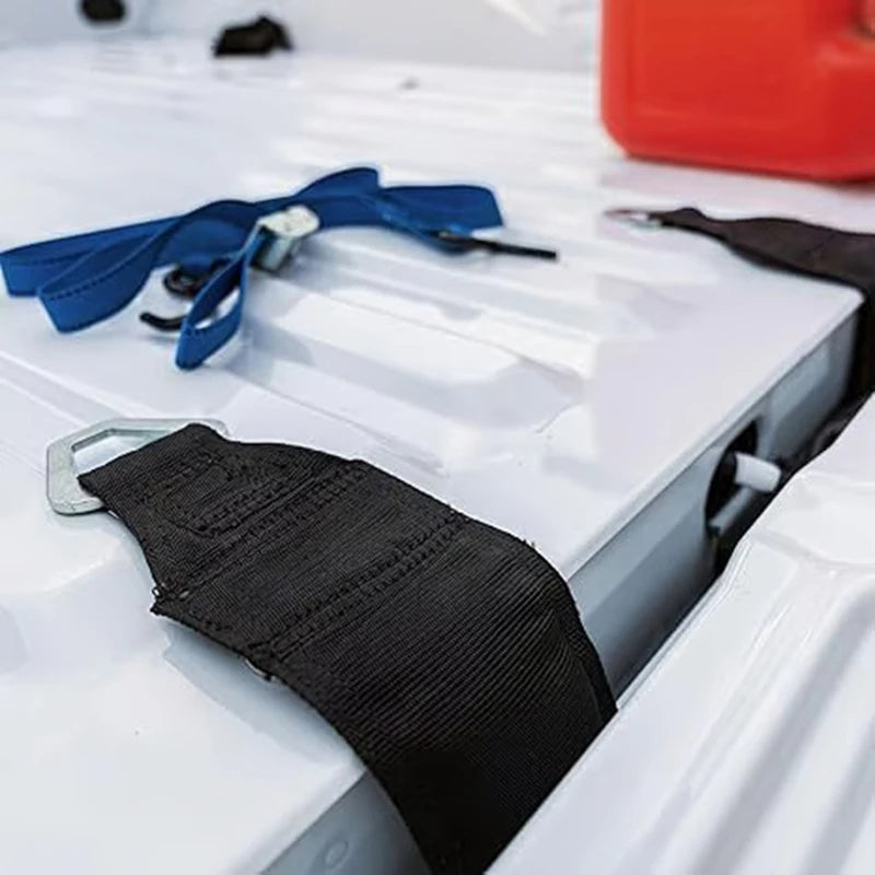 Black heavy-duty bed anchor strap and blue tie-down strap resting on a white surface.