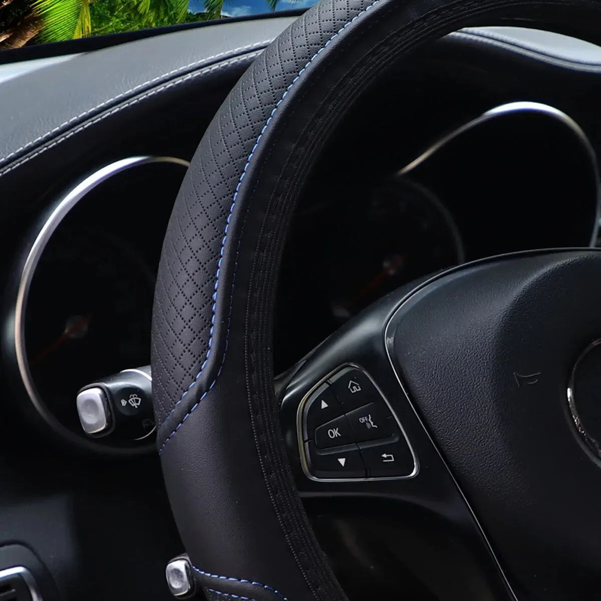 Close-up view of a black embossed leather steering wheel with blue stitching and controls.