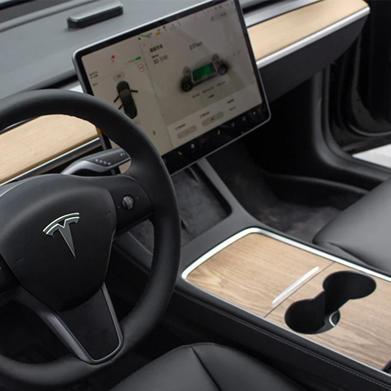 Interior view of a car dashboard showing a wood grain cover and a Tesla infotainment screen.