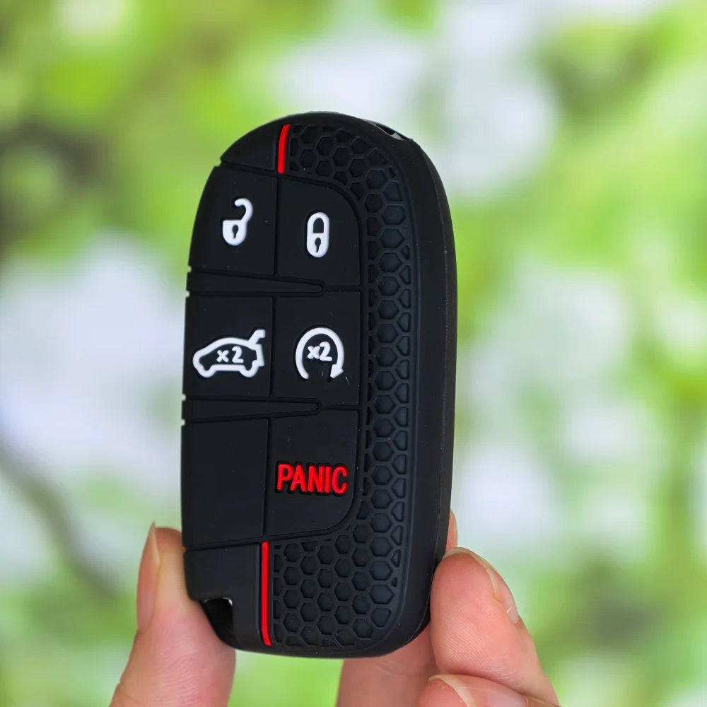 A black silicone car key cover for Jeep, Dodge, and Chrysler models is held in a hand against a blurred green background.